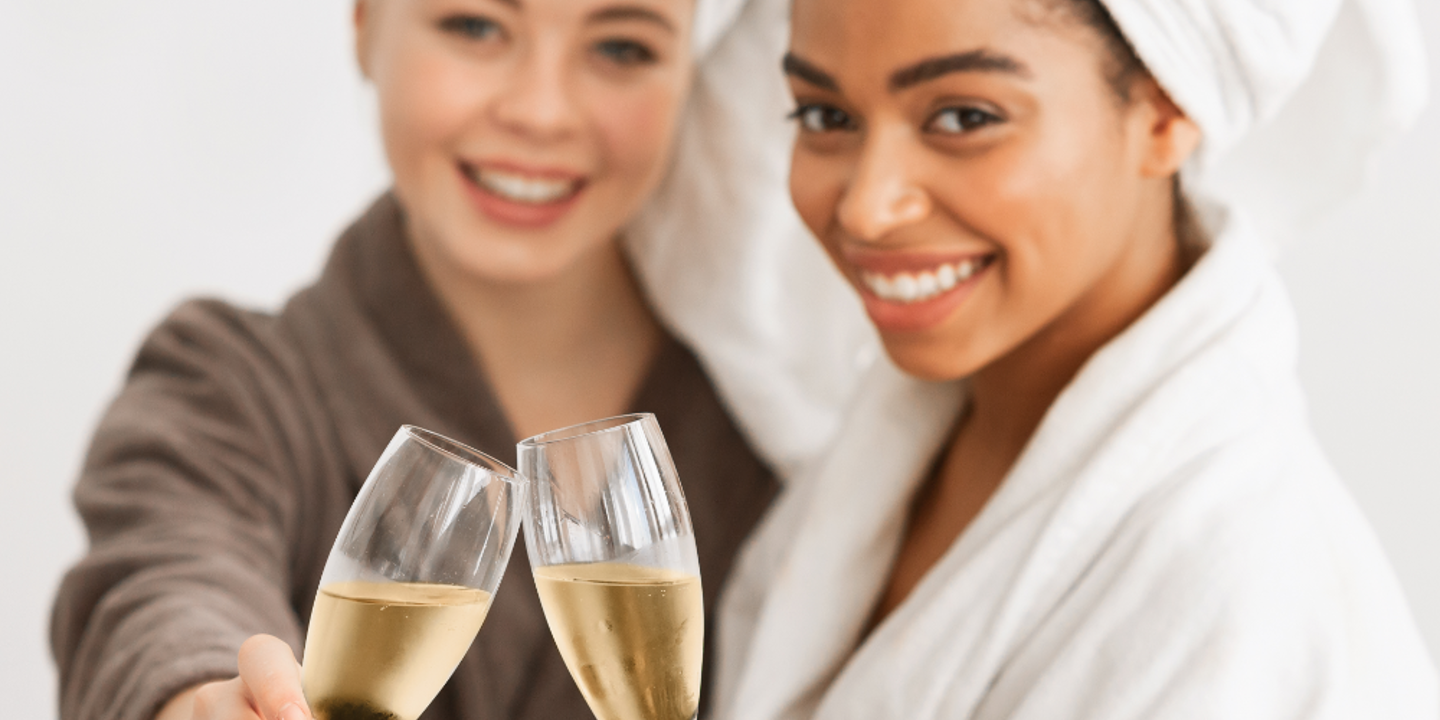 Two women wearing bath robes, each holding a champagne flute.