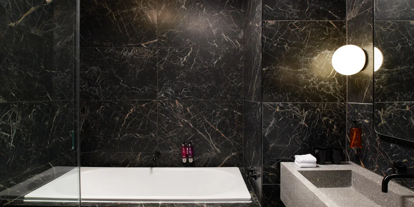Black and gold marble bathroom featuring bathtub, sink and mirror.