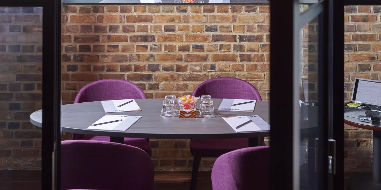 Table with purple chairs against a brick wall.
