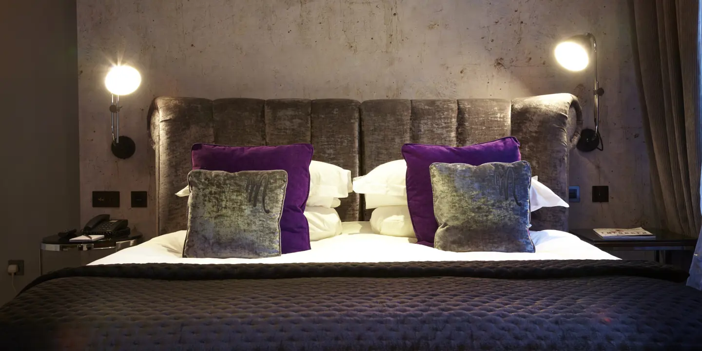 A bed adorned with two purple pillows and a pristine blanket.