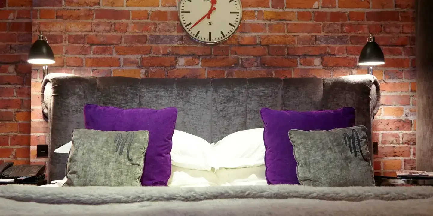 An elegantly made bed adorned with plush pillows and a wall-mounted clock.