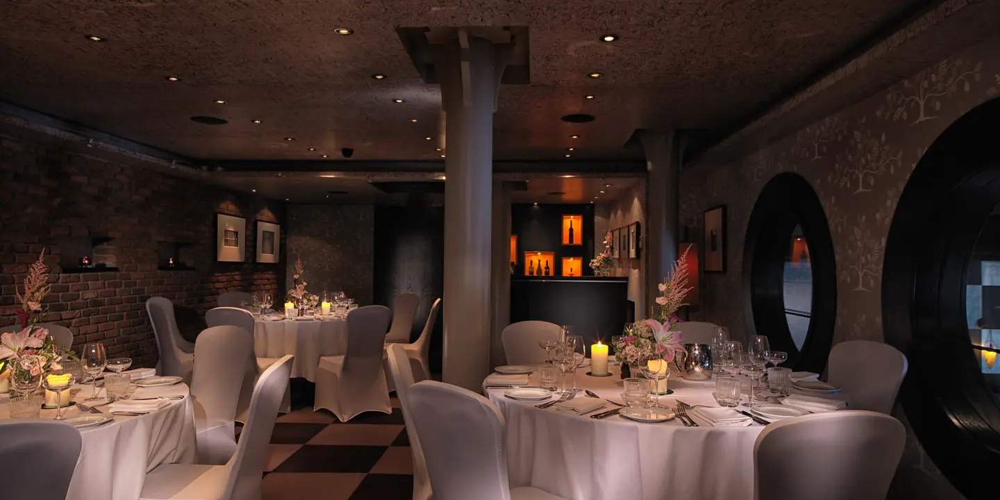 A private wedding dining room with round tables set for dinner and chairs adorned with white fabric covers.