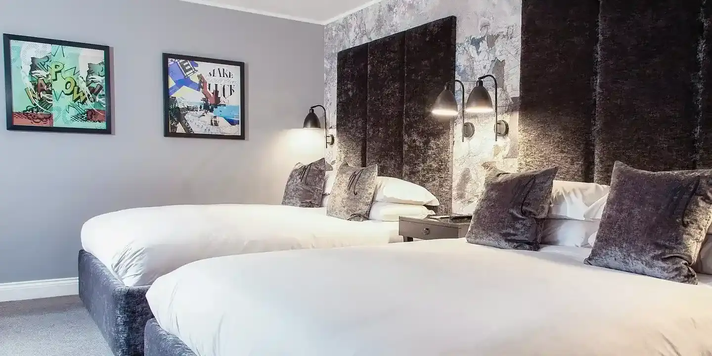 Two beds placed side by side with grey velvet headboards.