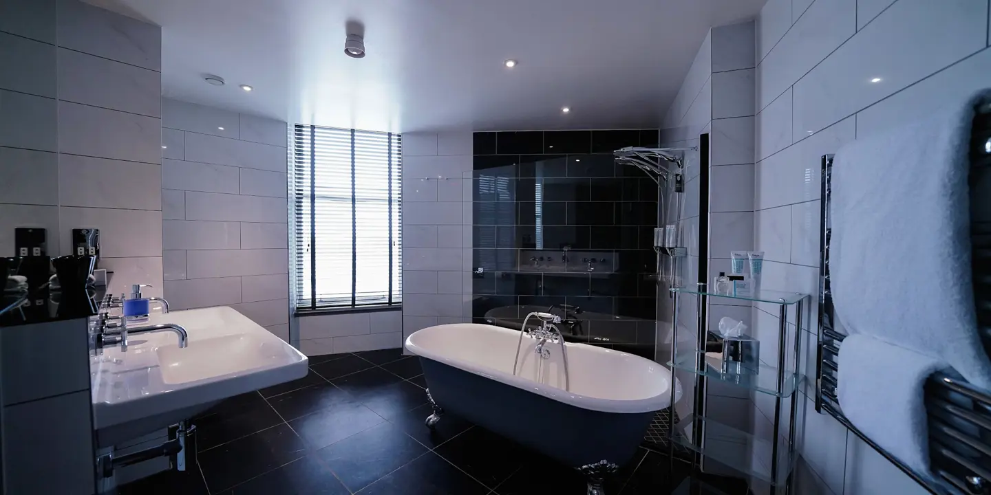 A black tiled bathroom with free standing bath, shower and dual sinks.