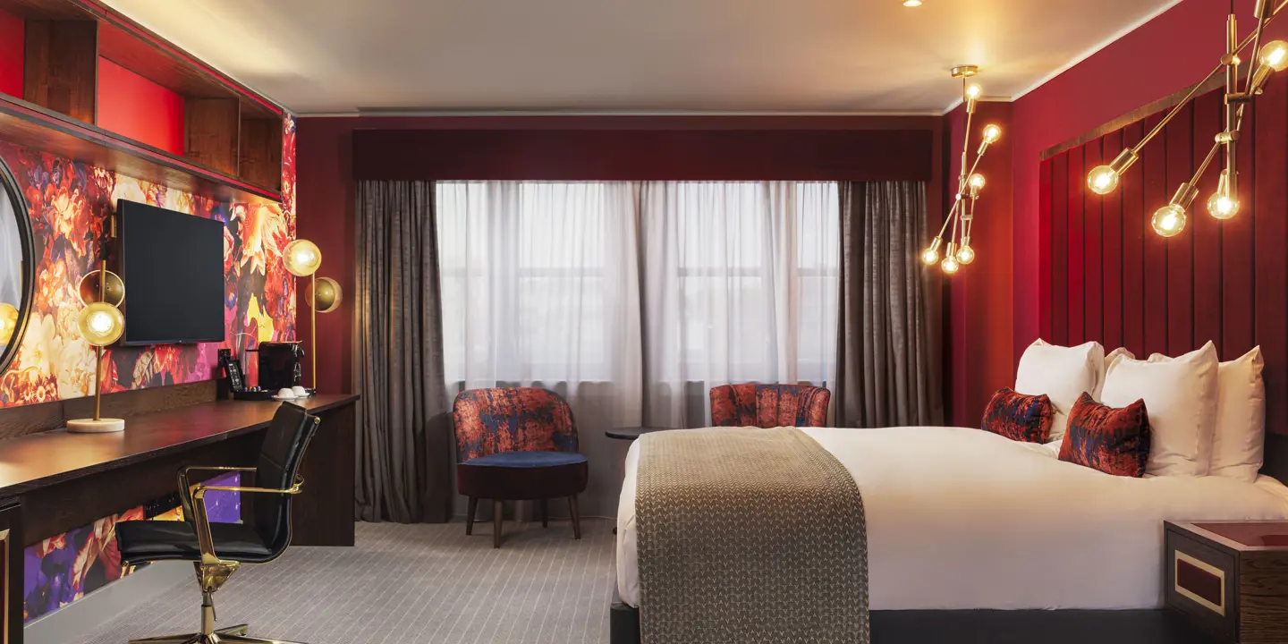 Spacious bedroom featuring a comfy bed, armchairs, work desk, mirror and wall mounted TV.