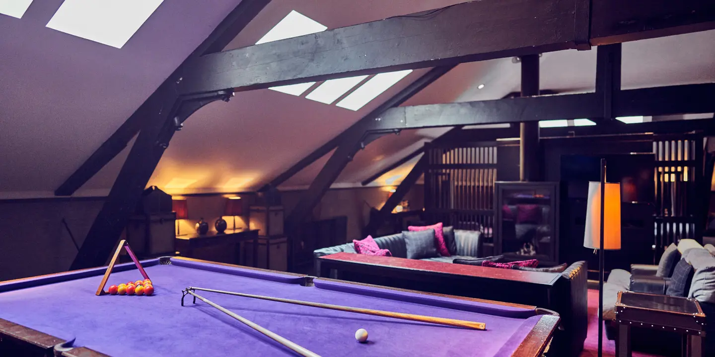 A darkly decorated room with a purple pool table and sofa. 