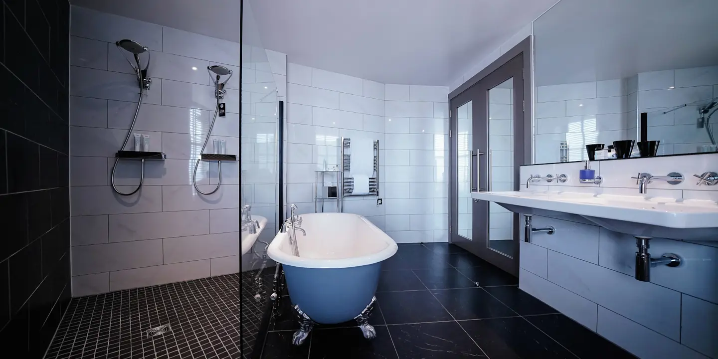 Black tiled bathroom with walk in shower, bathtub and dual sinks. 