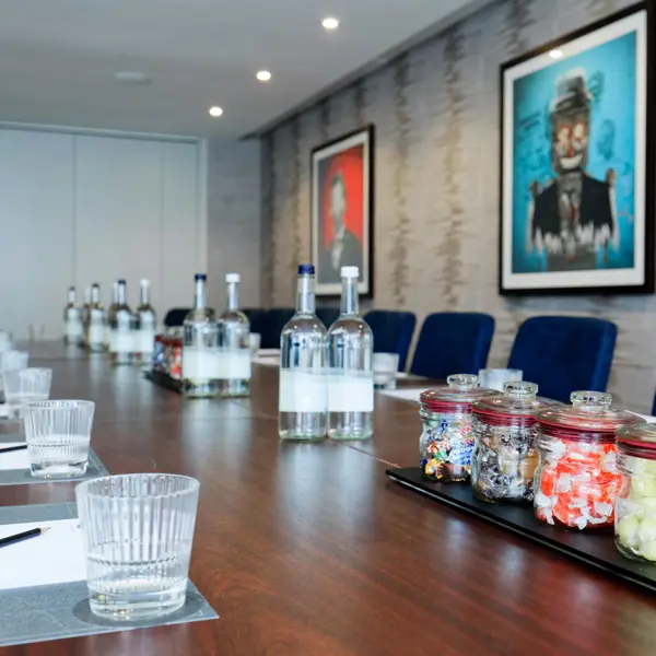 A close up photo of a meeting room table with drinking glasses, writing pads and pencils, and 4 glass jars with boiled sweets inside them