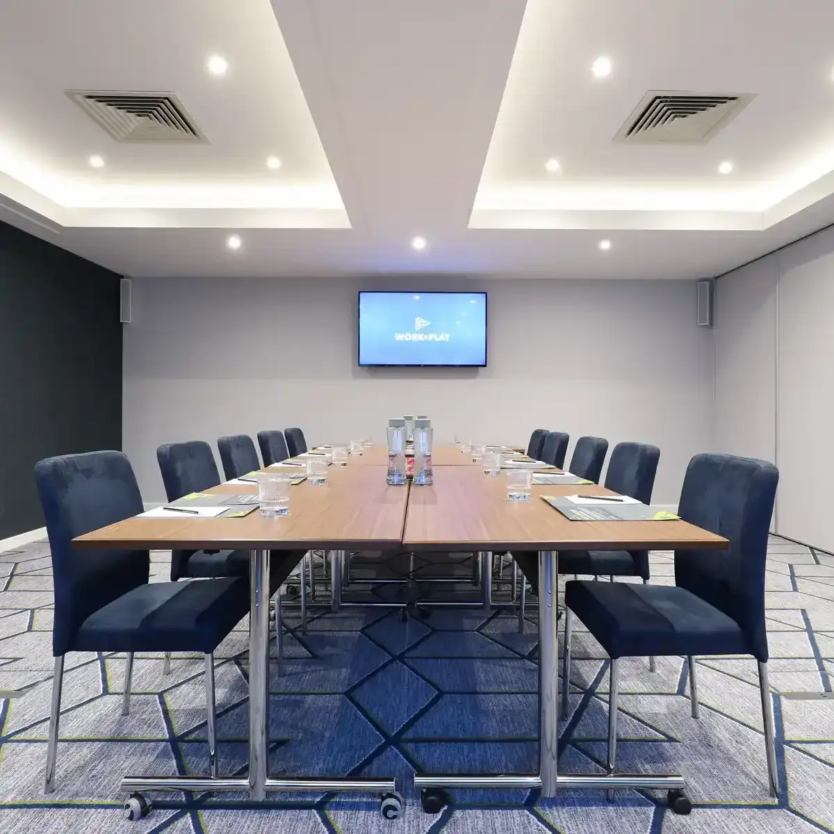 Conference room featuring a spacious table and chairs, grey carpet and flat screen TV.