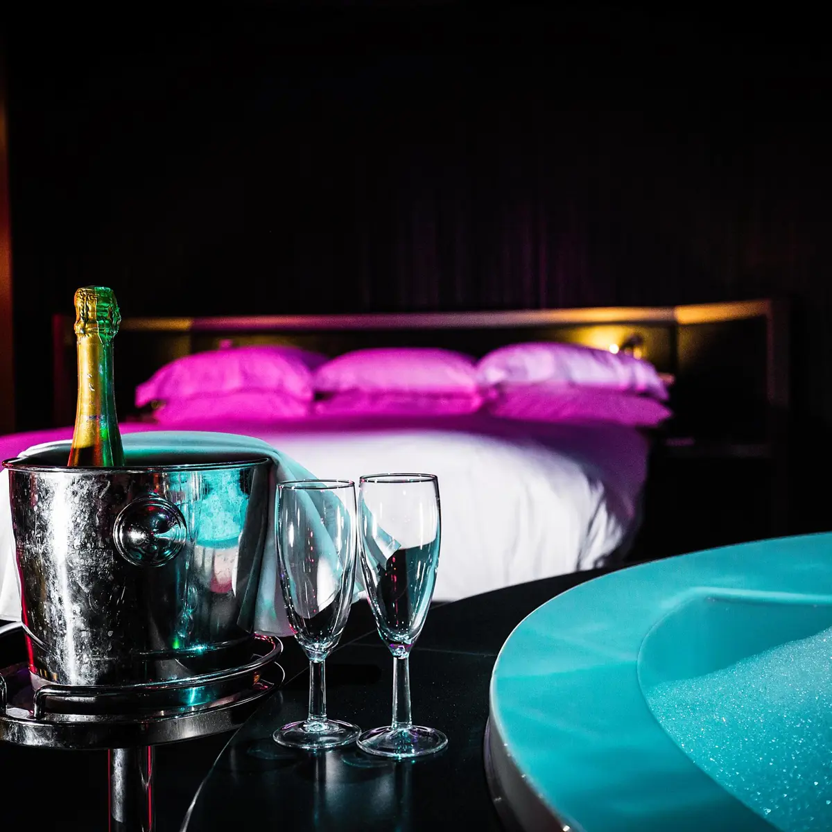 Table with champagne and 2 champagne glasses in front of a bed.