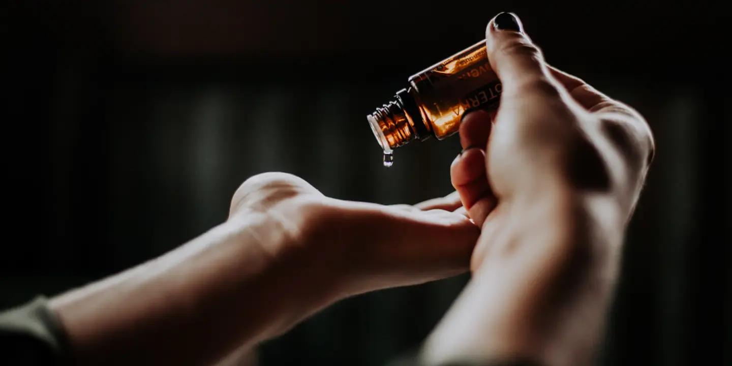 An individual using a bottle of oil on their hands.