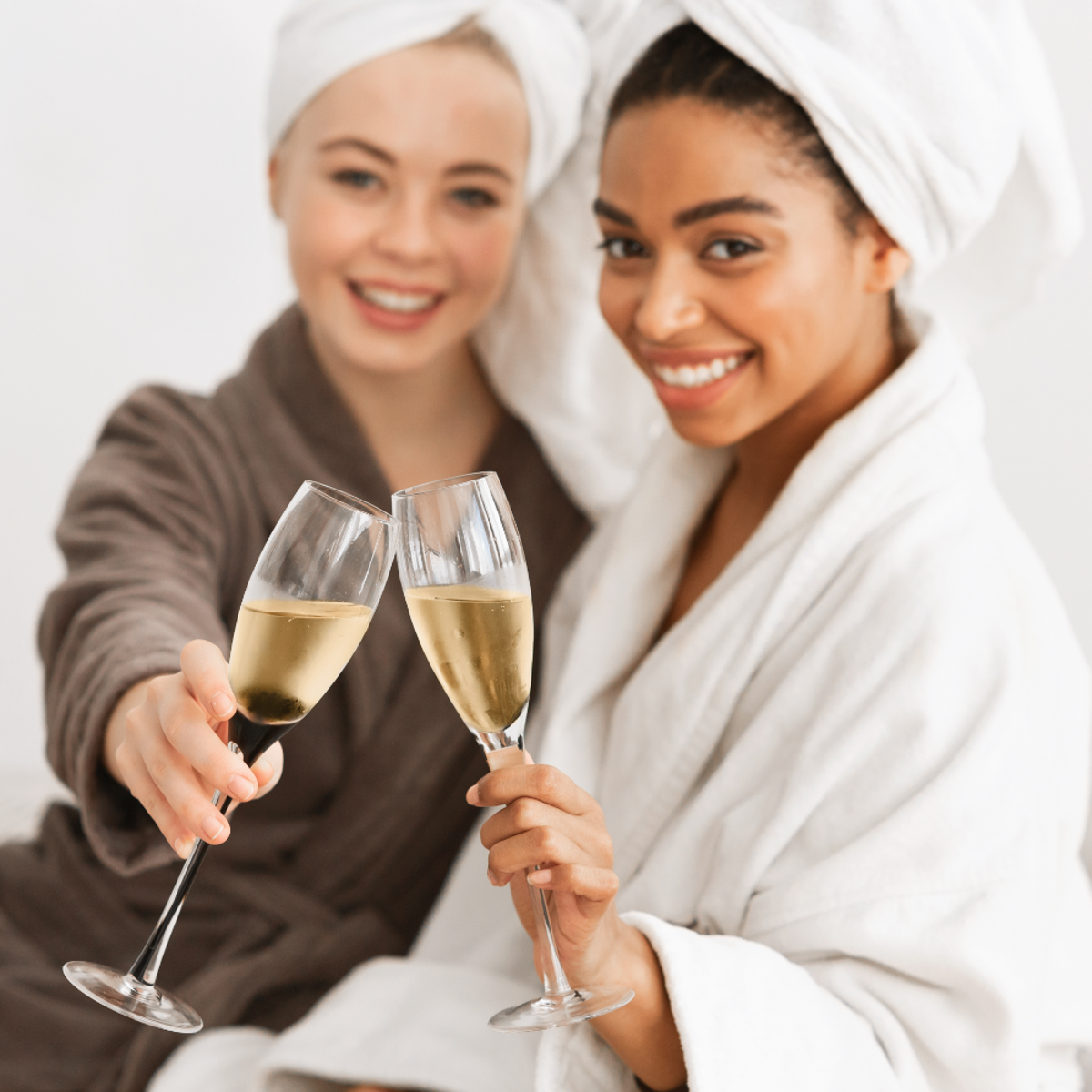 Two women wearing bath robes, each holding a champagne flute.