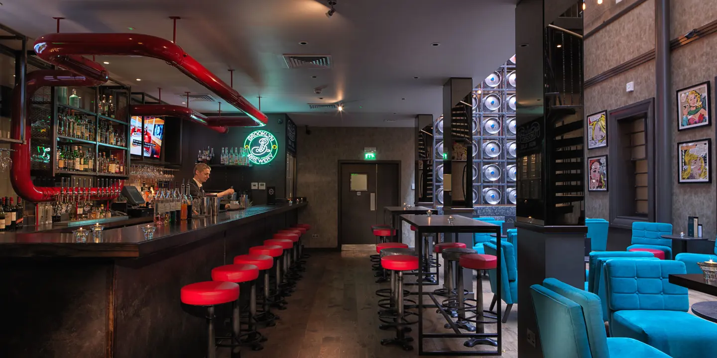 An establishment featuring a bar area adorned with blue chairs and red stools.