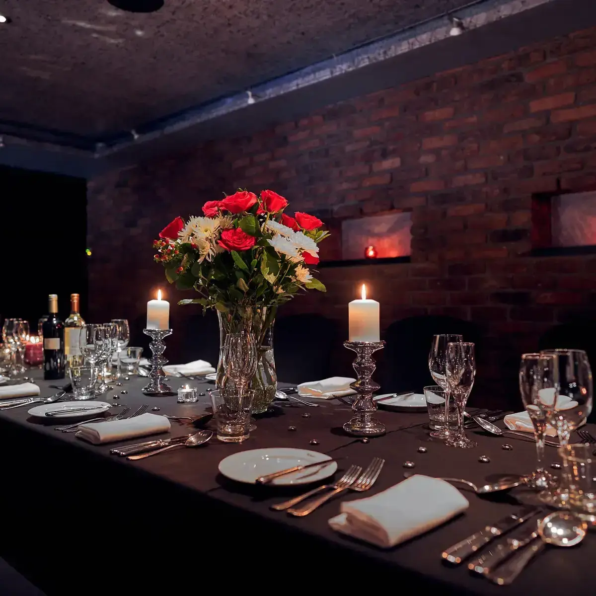 Private dining room featuring a table laid for dinner service, white candles in silver candlesticks, and a red and white floral centrepiece.