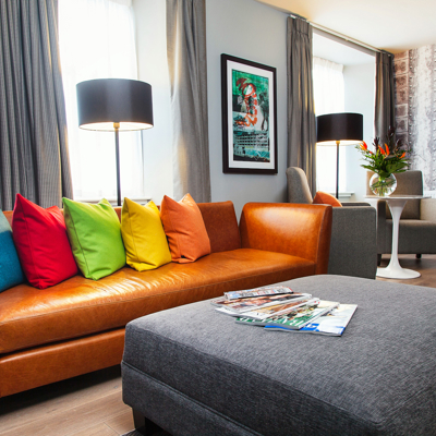 A brown leather sofa lined with multi-coloured cushions.