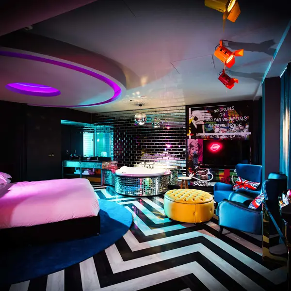 A well-furnished brightly coloured room featuring a bed, a cozy chair, and a disco ball decorated bath.
