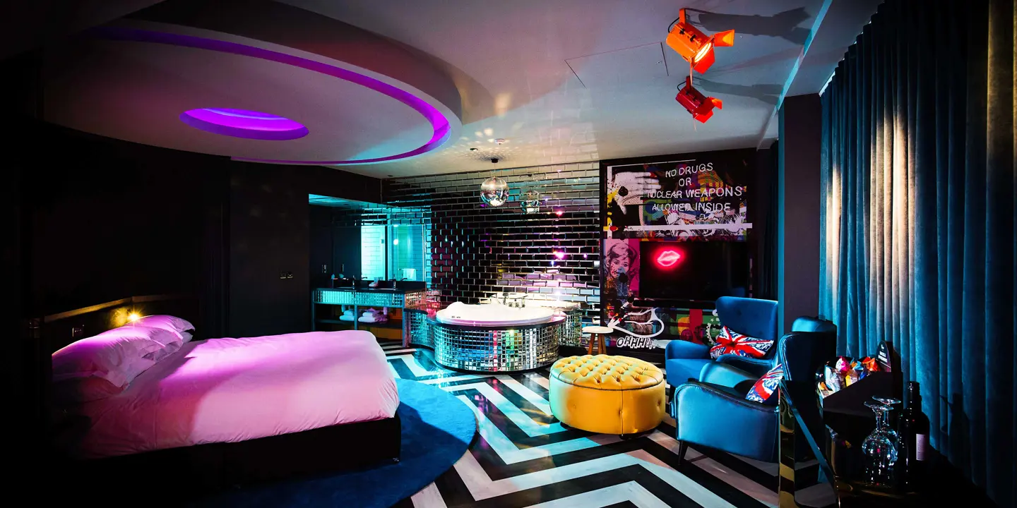A well-furnished brightly coloured room featuring a bed, a cozy chair, and a disco ball decorated bath.