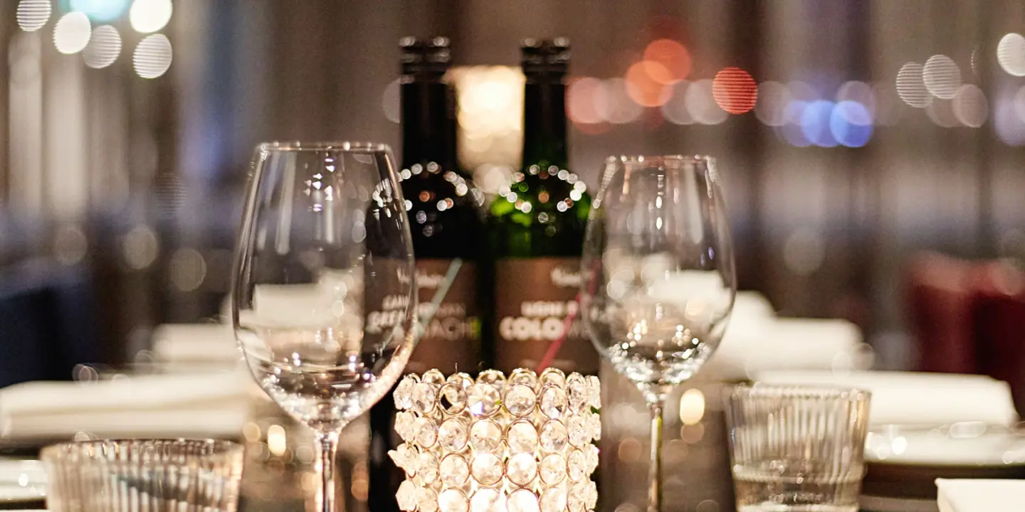 A table with 2 wine glasses, an elegant candle and two bottles of wine.
