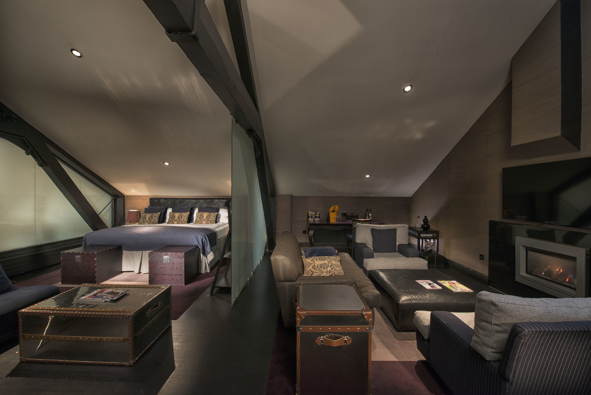 An elegantly furnished bedroom featuring a comfortable bed, stylish chair, functional desk, and modern television.