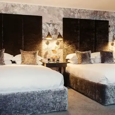 Two beds placed side by side with grey velvet headboards.