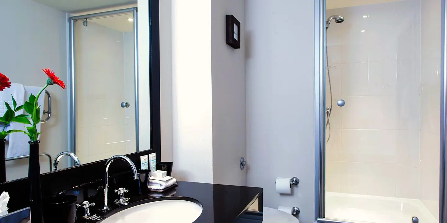 A black and white bathroom with shower, sink, toilet and mirror.