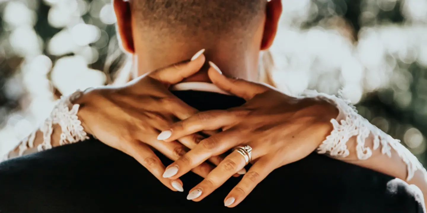 Close-up of a person hands resting on someones shoulders wearing a wedding ring.