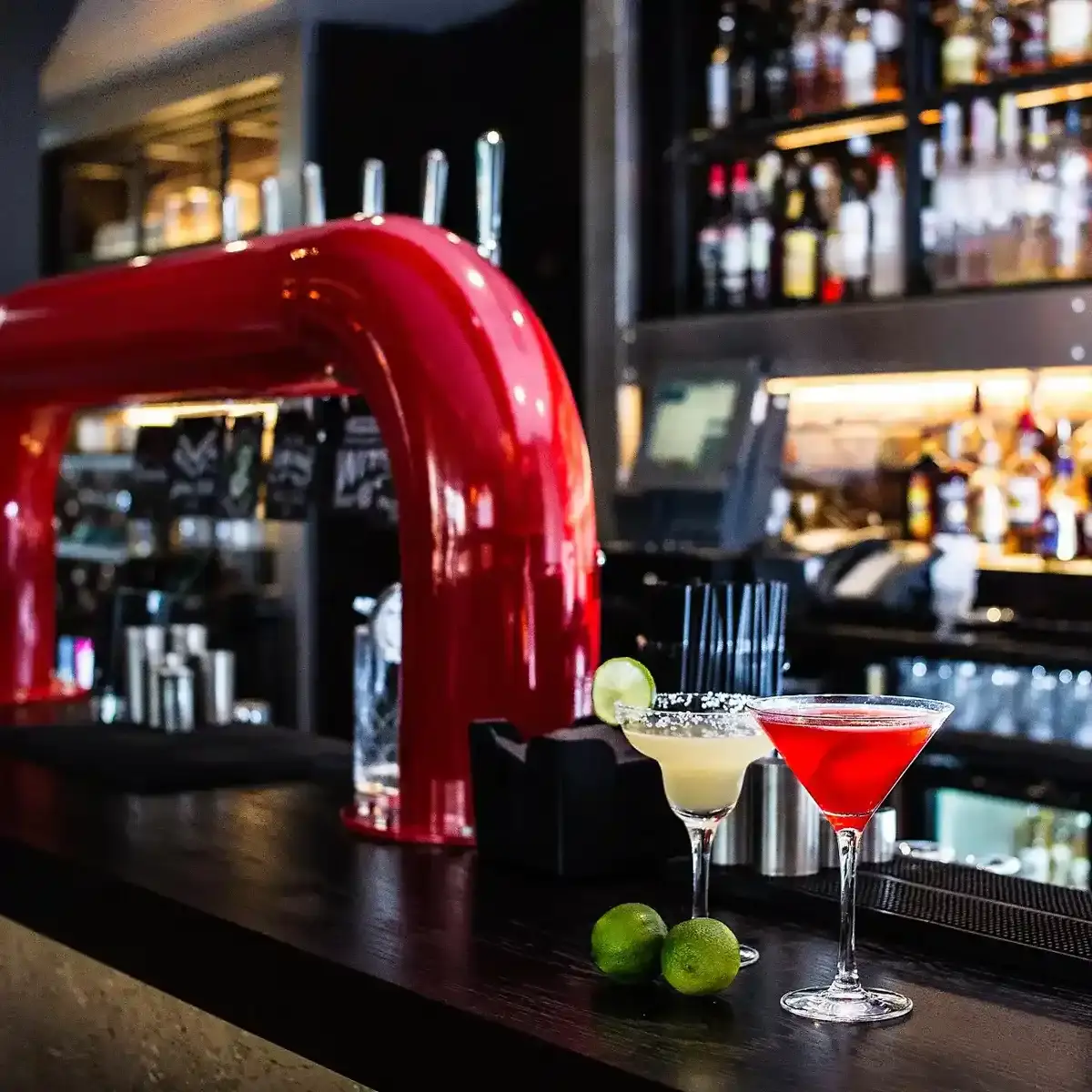 Two cocktail glasses placed on a bar counter with slices of lime.