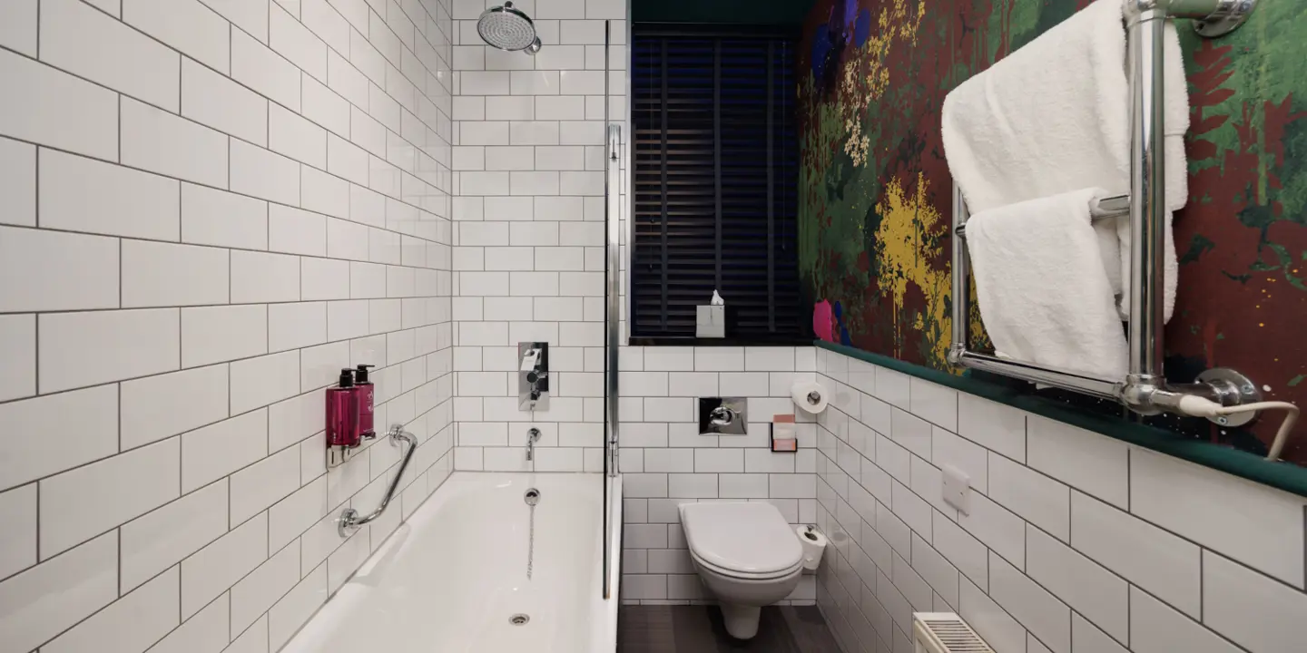 Black tiled bathroom featuring a bath, sink and mirror.