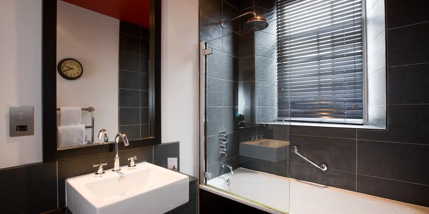 Black tiled bathroom featuring a bath, sink and mirror.