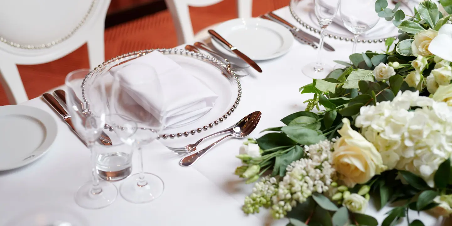 A table elegantly arranged for a formal dinner, adorned with white flowers and silverware.