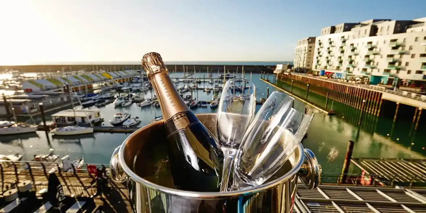 A bottle of champagne resting in an elegant bucket alongside silver spoons.