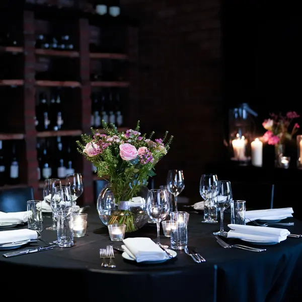 Table set for a formal dinner with wine bottles in the background.