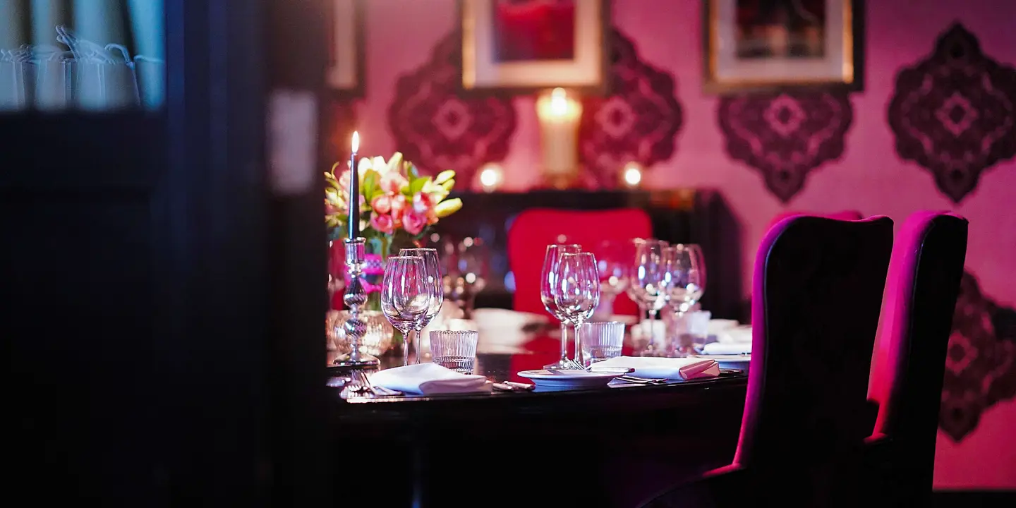 A private dining room with a table featuring several wine glasses, lit candles, flower centrepiece and deep pink seating