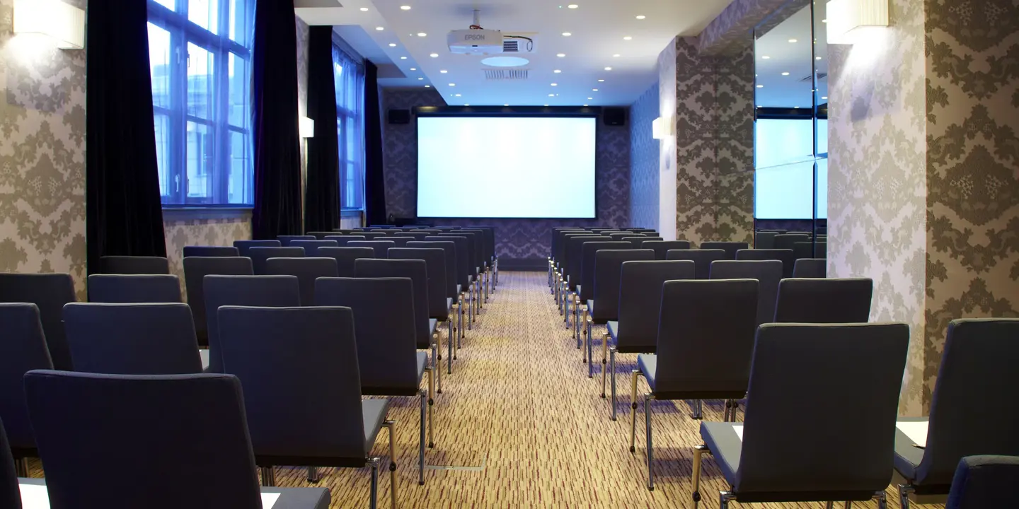 An auditorium with neatly arranged rows of chairs and a large projector screen.