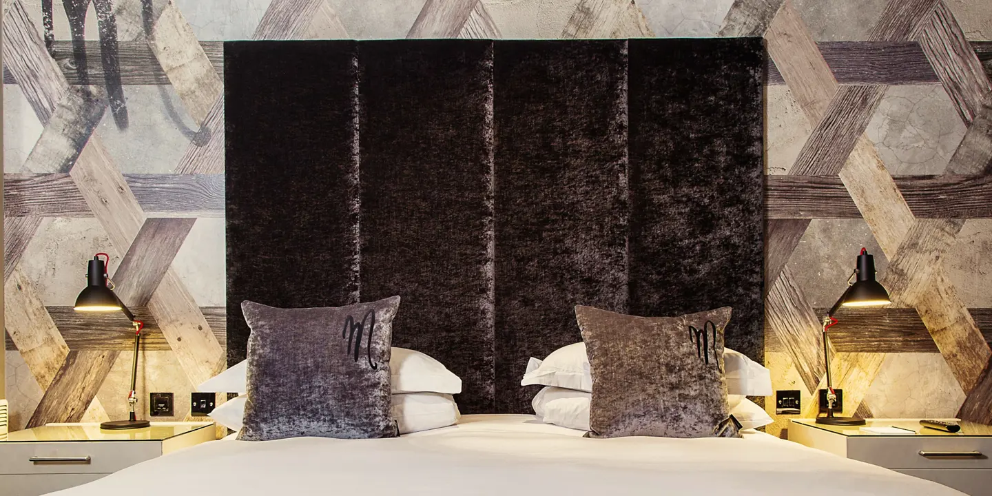 A bed featuring a grey velvet headboard adorned with grey plush pillows.