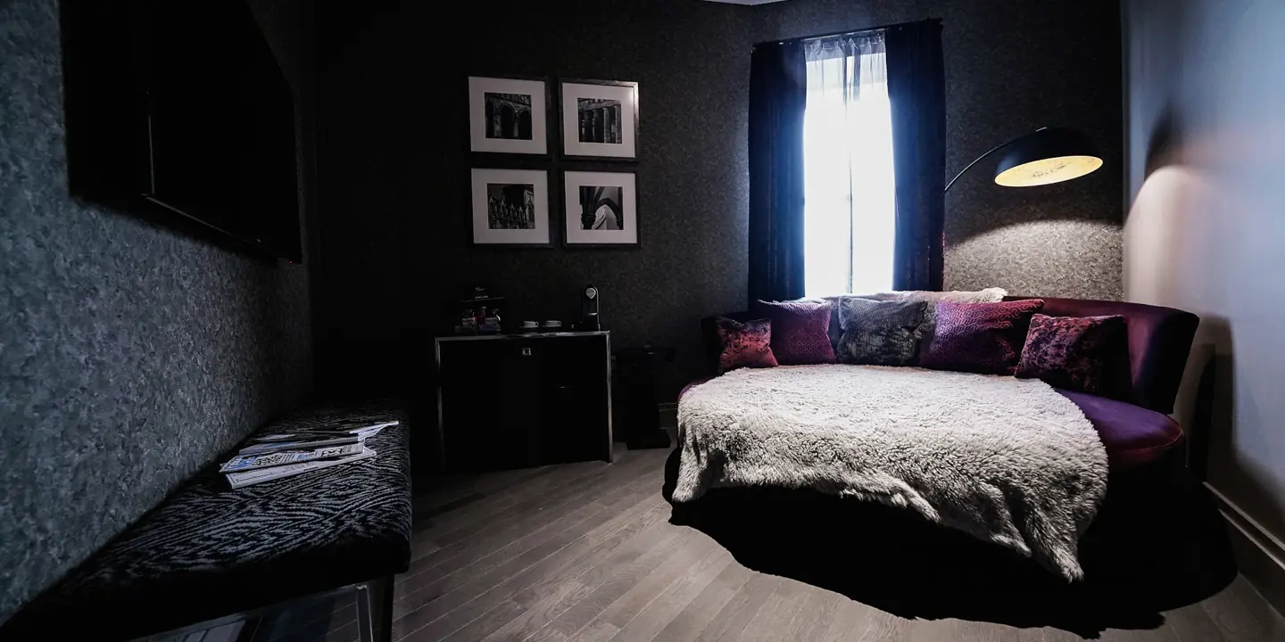 Darkly decorated bedroom, with purple velvet sofa with purple pillows.