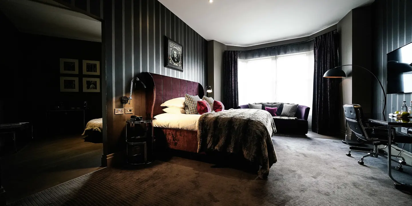 A large red velvet bed placed in the middle of the room with a sofa, desk and tv.