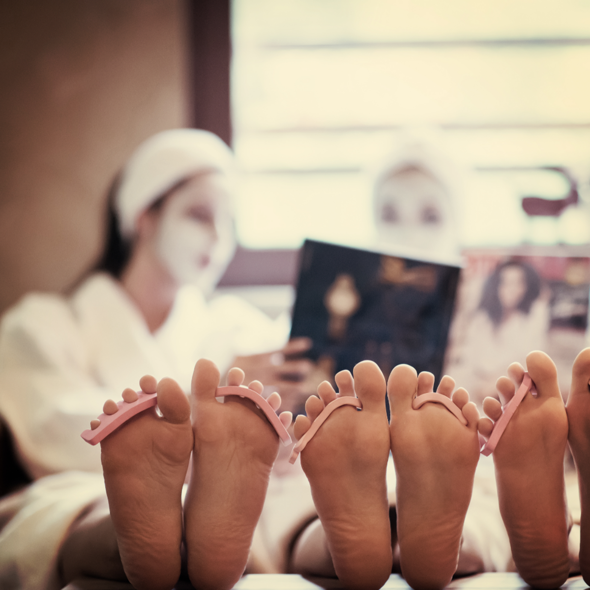 Three women relaxing on a bed in spa robes with their feet elevated.