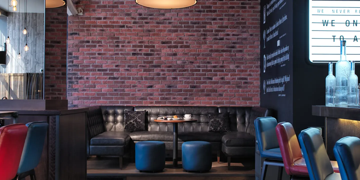 Exposed brick feature wall in the Malmaison Birmingham bar. A black leather sofa is visible with a round table and two blue stools.