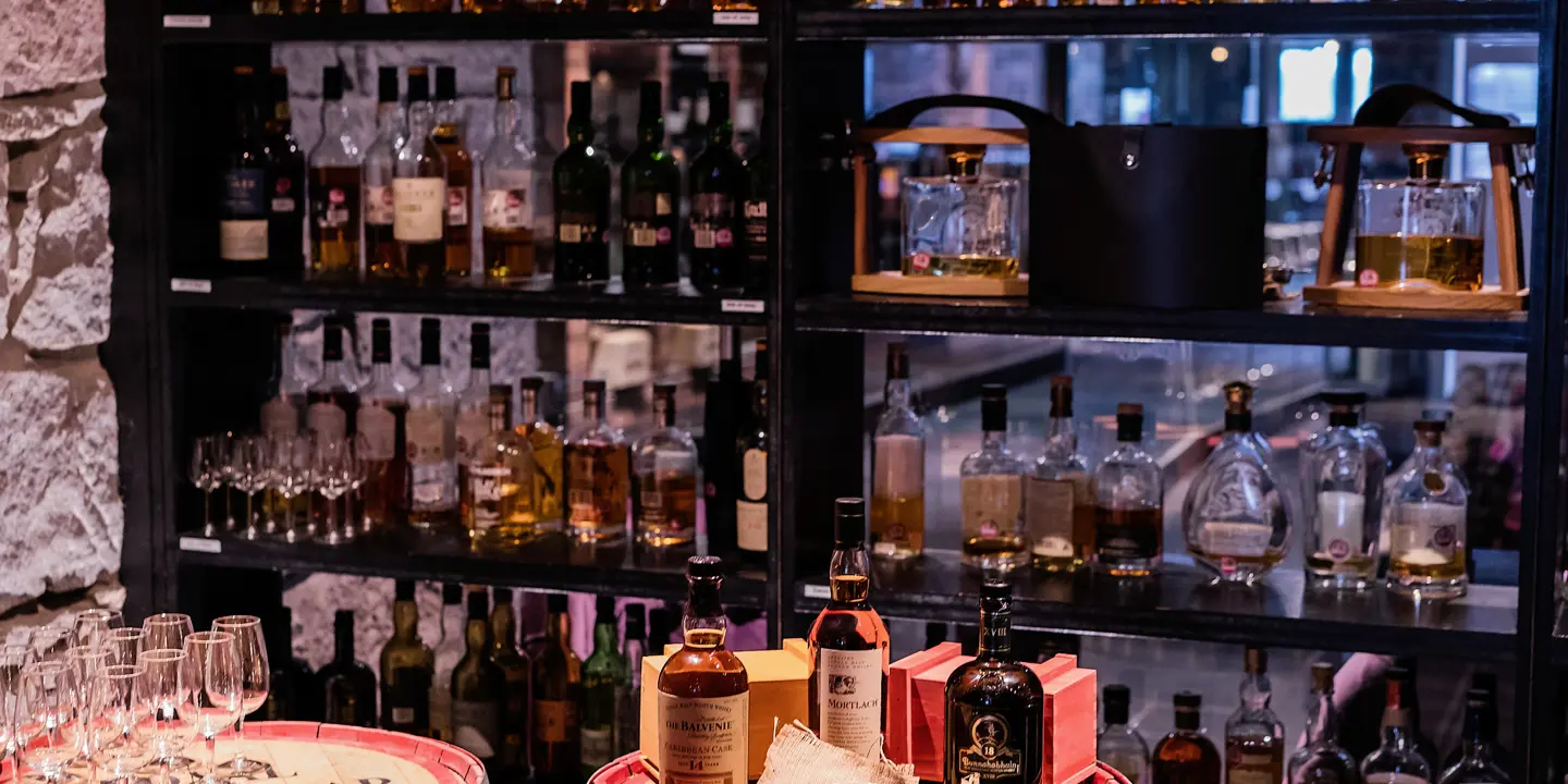 A range of whiskies on a mirrored shelving unit and additional bottles and glasses on top of two whisky barrels.