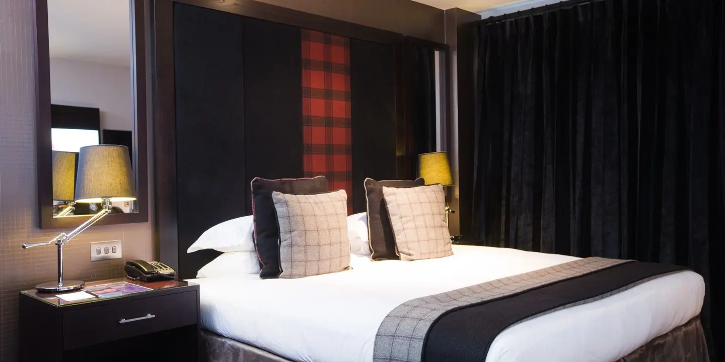 An elegantly furnished hotel room featuring a comfortable bed and bedside table with a lamp.