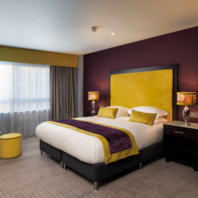 An elegantly furnished hotel room featuring a comfortable bed and bedside table with a lamp.