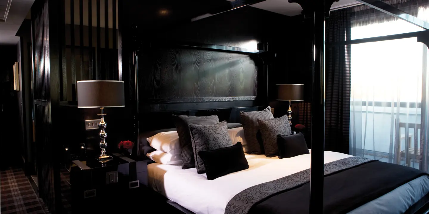 A black wooden bed adorned with multiple black cushions.