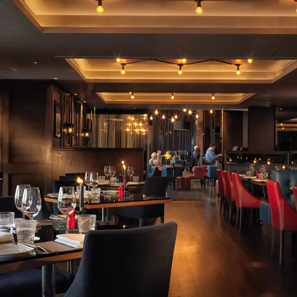 Birmingham Malmaison restaurant interior featuring grey and red seating, tables adorned with candles, glasses, and silverware.