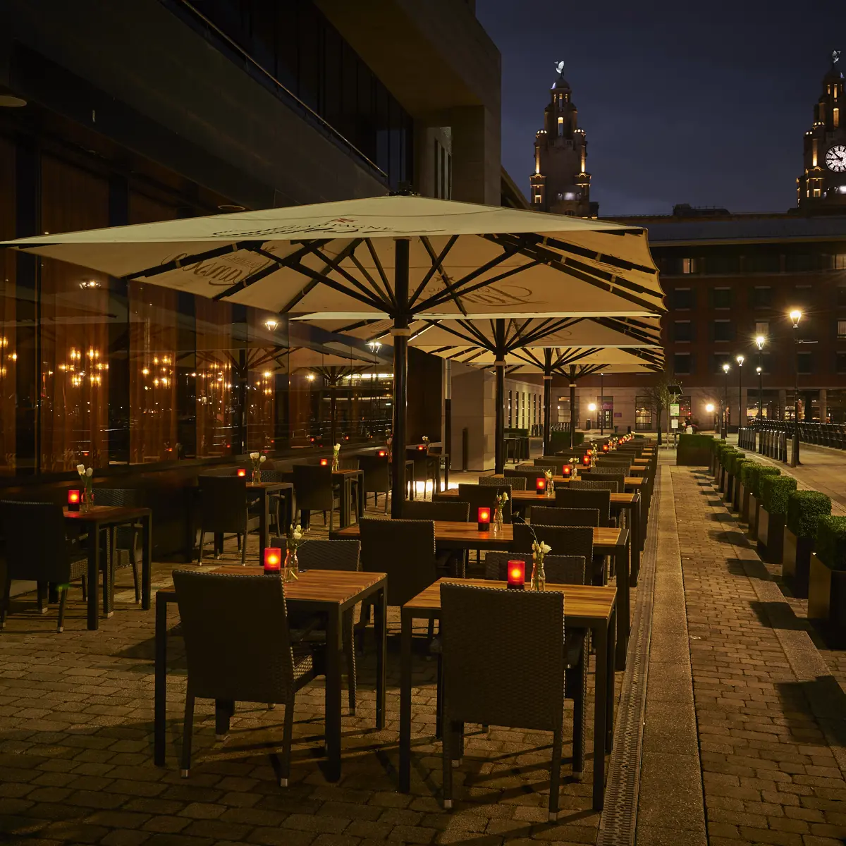 An illuminated restaurant featuring tables and umbrellas during nighttime.