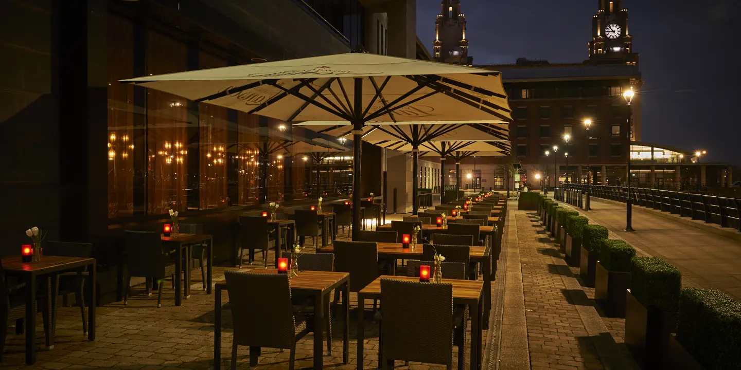 An illuminated restaurant featuring tables and umbrellas during nighttime.