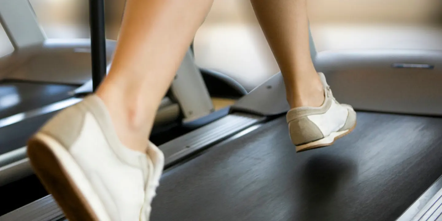 Close up of a persons lower legs wearing grey and white sneakers, running on a treadmill