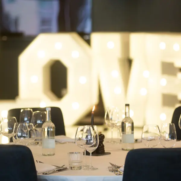 A table arranged with wine glasses and place settings. A light display in the background spells out the word love