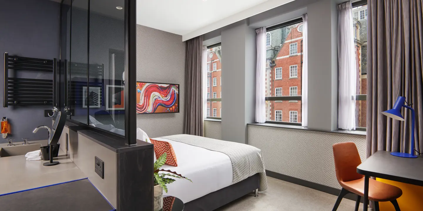 An elegantly furnished hotel room featuring a comfortable bed, spacious desk, and huge windows. 