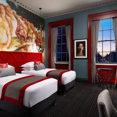 Two beds and a wall painting in a vibrant red hotel room.